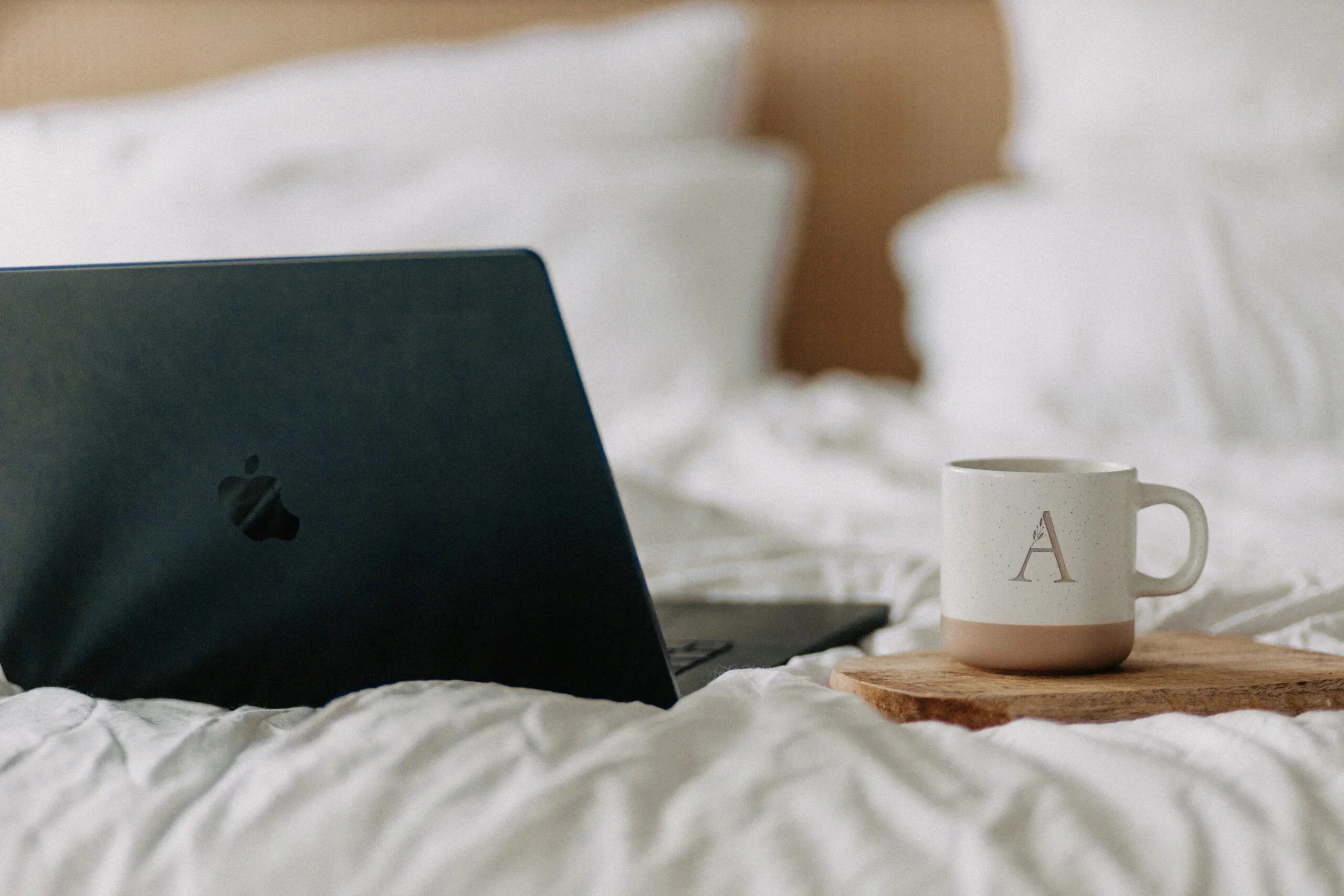Aufgeklappter Laptop und Tasse auf einer hellen Bettdecke
