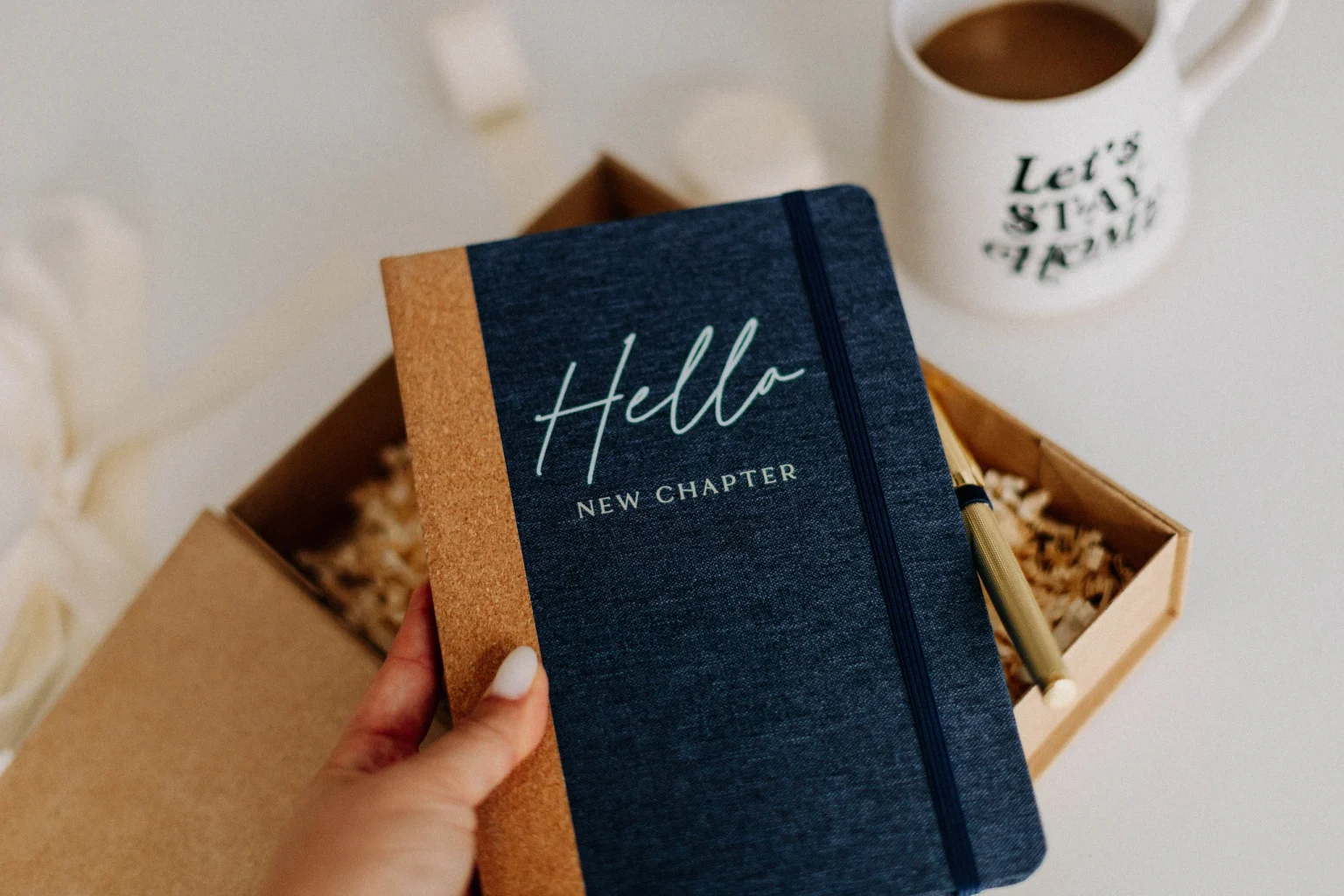 Eine Hand hält das navyblaue Notizbuch Hello New Chapter über die geöffnete Box