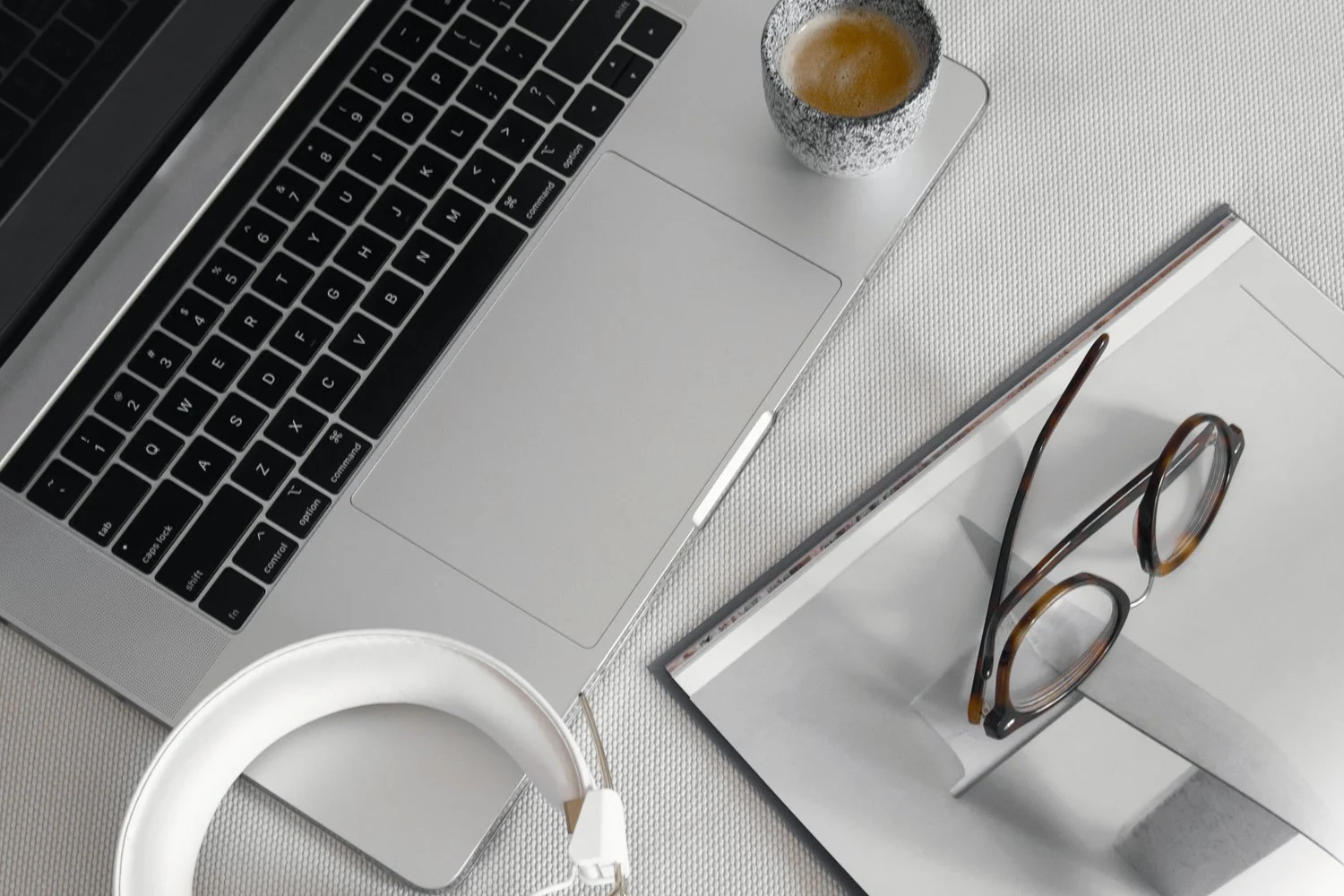 Laptop, Kopfhörer, Brille und Kaffee auf einem hellen Arbeitsplatz von oben