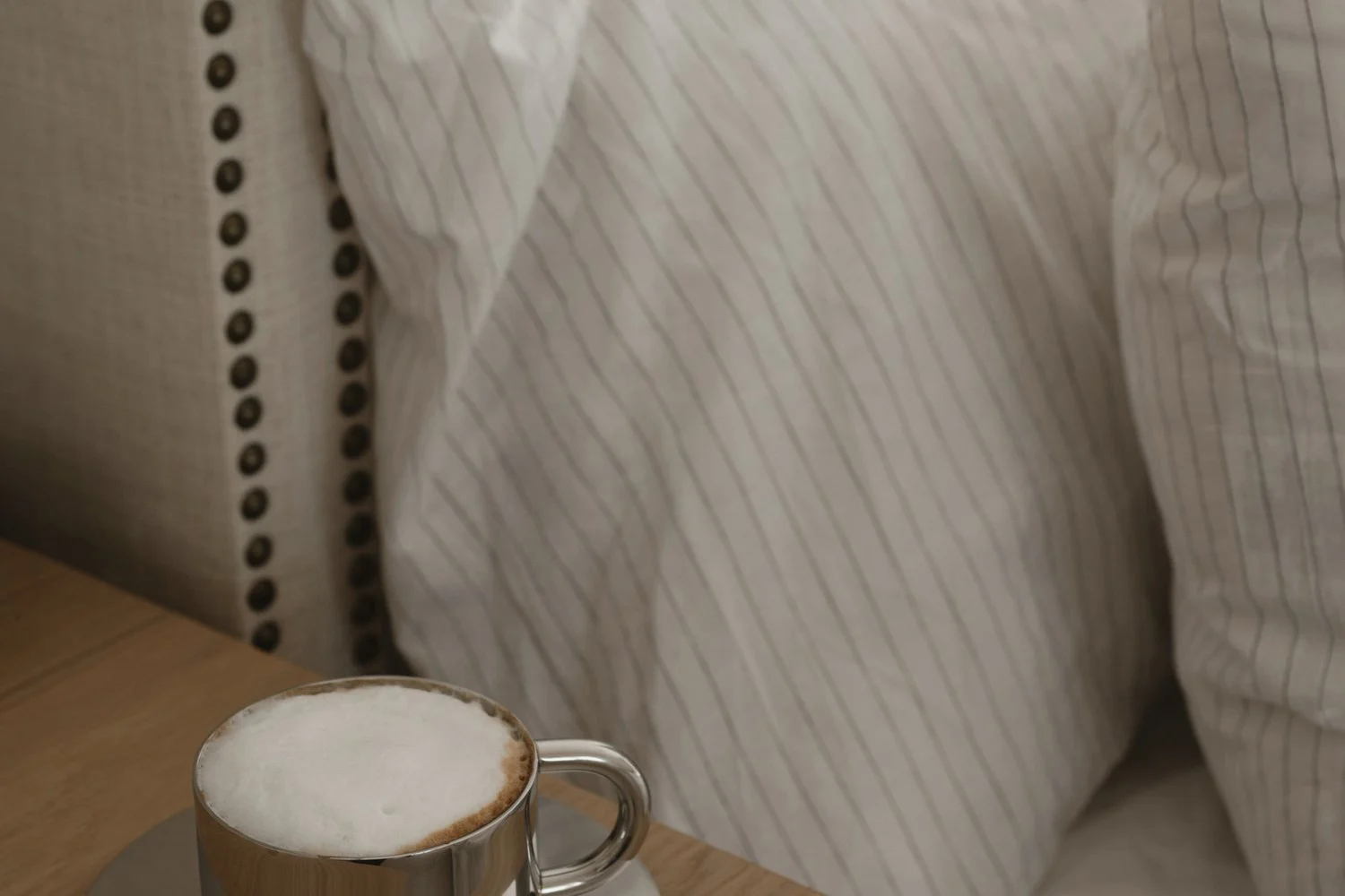 Kaffeetasse auf dem Nachttisch neben hellen Kissen
