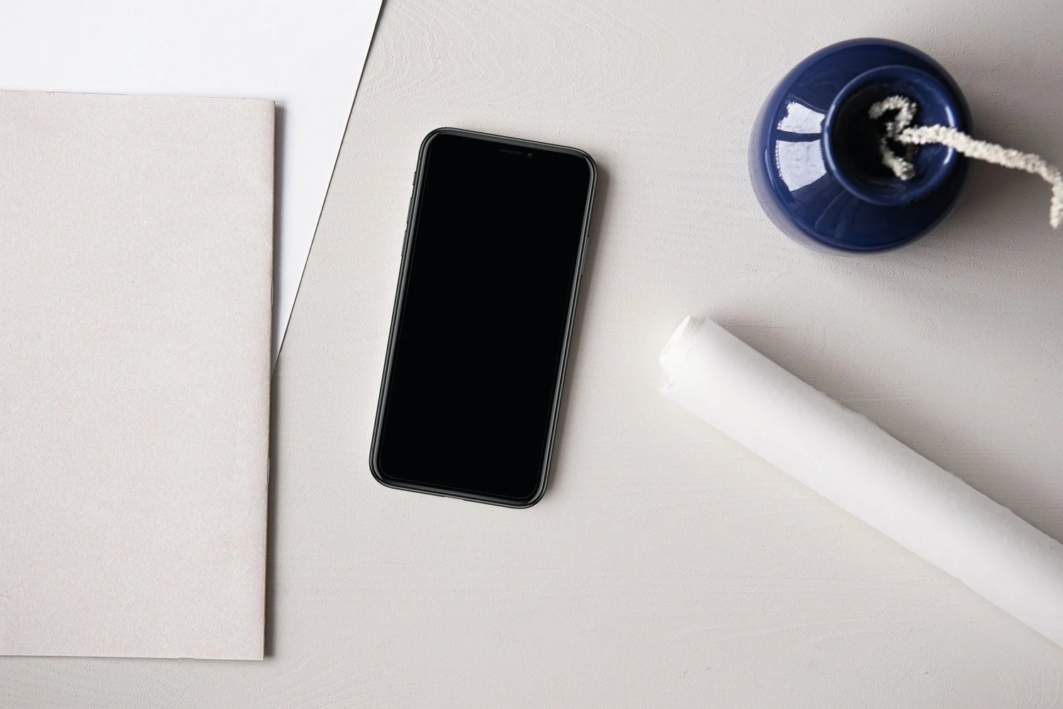Smartphone, Notizblock und navyblaue Vase auf einem hellen Schreibtisch