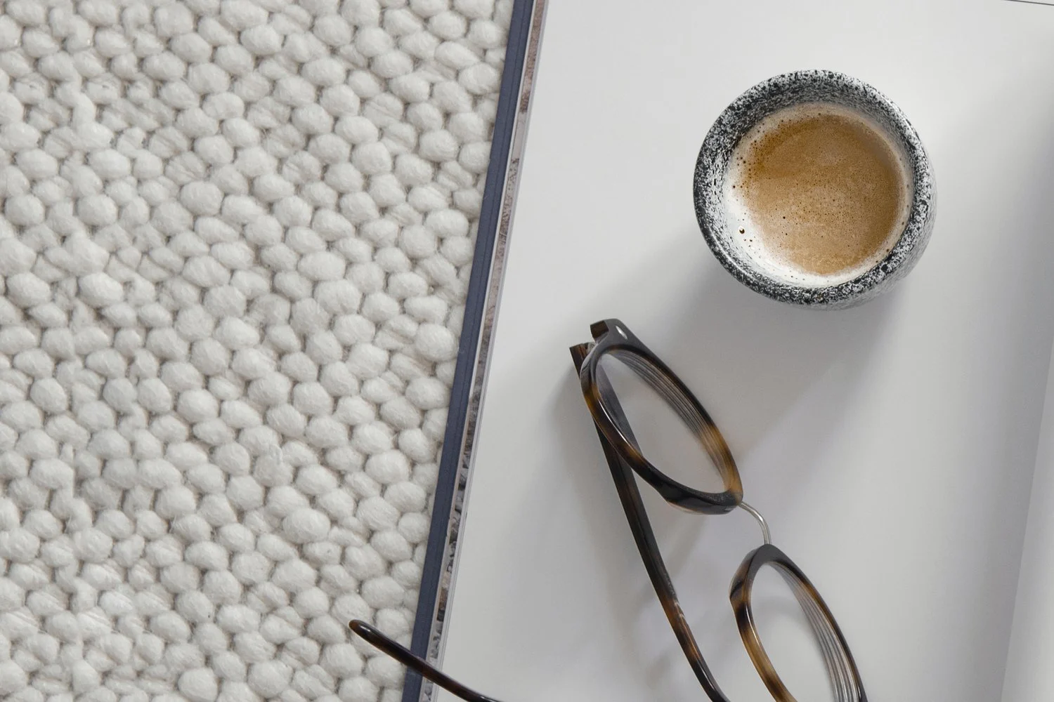 Tablett mit Kaffee, Brille und Notizbuch auf einer Strickdecke