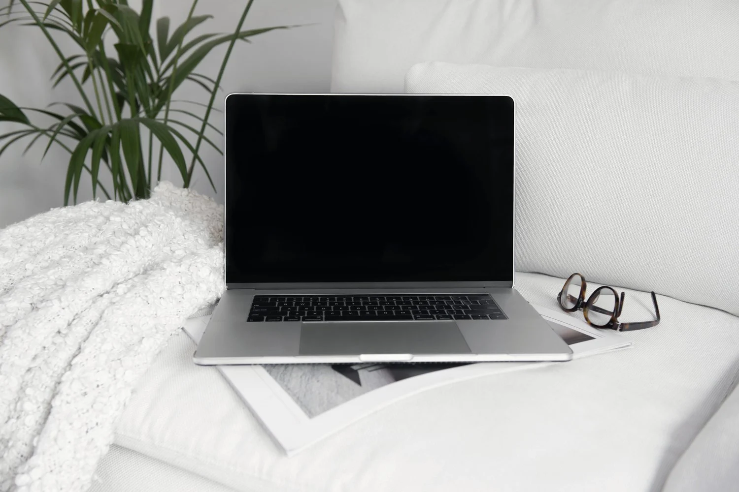 Aufgeklappter Laptop mit Brille auf einem hellen Sofa